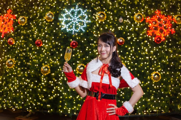 Heureuse fille souriante de Santa est mignonne en costume rouge et main tenant champagne