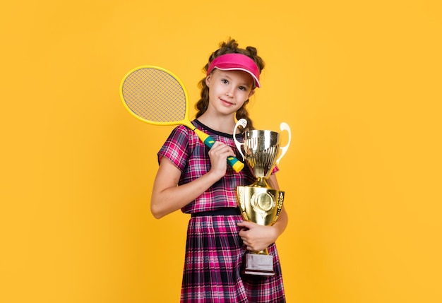 Heureuse fille tenant un équipement de sport enfant tenir une raquette de tennis enfant porter une casquette de fitness activité de l'enfance mode de vie sain être énergique joueur de badminton avec vainqueur du champion de la coupe du championnat