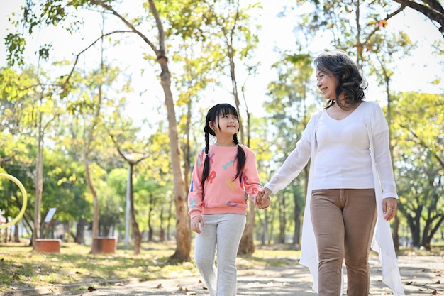 Heureuse grand-mère asiatique tenant la main de sa petite-fille en marchant ensemble dans le parc