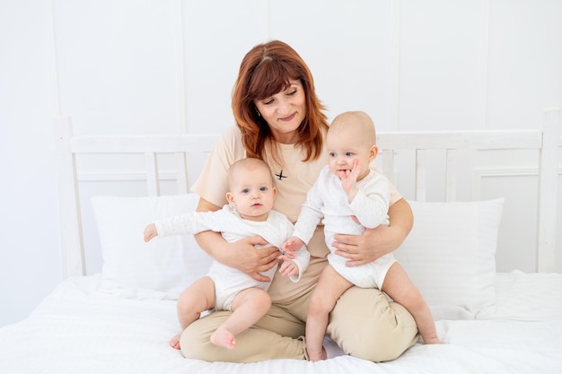 Heureuse grand-mère avec deux petits-enfants bébé à la maison sur le lit câlins et bisous