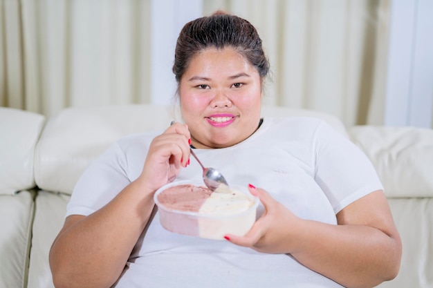 Heureuse grosse femme mangeant de la glace sur le canapé