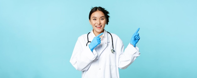 Heureuse infirmière souriante femme médecin asiatique pointant vers la droite montrant la publicité de la clinique promotionnelle debout je