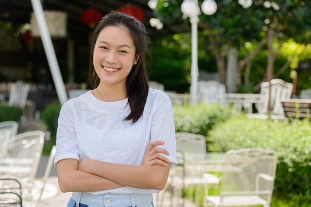 Heureuse jeune belle femme asiatique avec les bras croisés au café en plein air