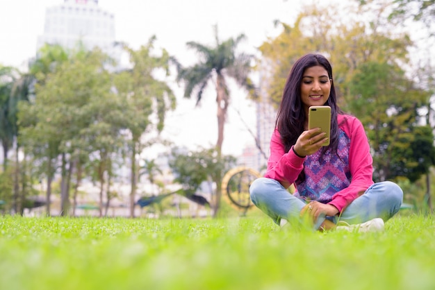 Heureuse jeune belle femme persane à l'aide de téléphone dans le parc