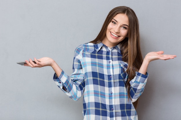 Heureuse jeune belle femme souriante aux cheveux kong en chemise à carreaux tenant un téléphone portable et un fond sur les paumes