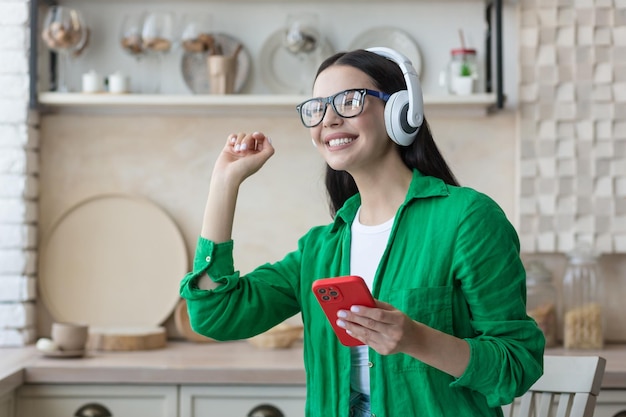 Heureuse jeune belle femme en vêtements verts et lunettes écoutant de la musique dans des écouteurs blancs sur