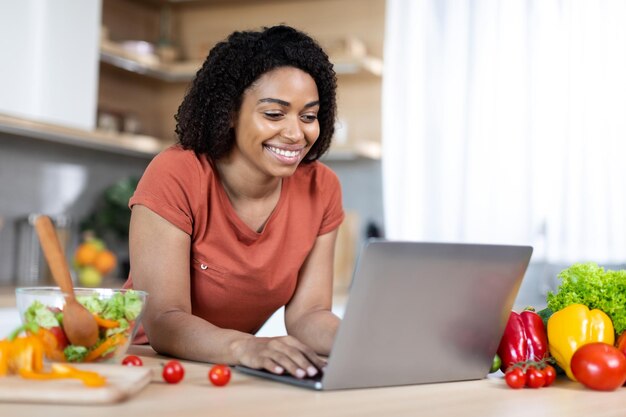 Heureuse jeune blogueuse afro-américaine tapant sur un ordinateur portable avoir un chat en ligne