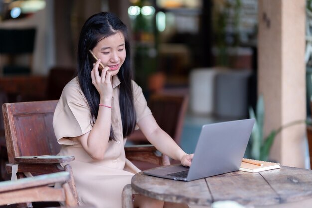 Photo heureuse de jeune étudiante adolescente asiatique en train de parler en utilisant un smartphone, en utilisant un ordinateur portable, en utilisant l'éducation en ligne, le concept d'apprentissage en ligne, les gens indépendants, les femmes d'affaires.