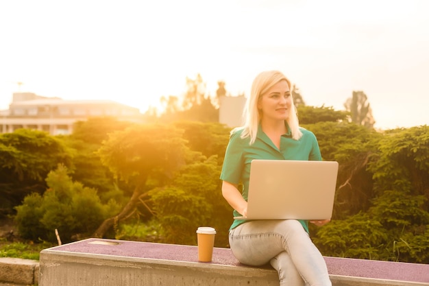 heureuse jeune étudiante femme avec ordinateur portable dans l'étude du parc de la ville