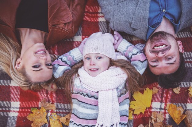 Heureuse jeune famille allongée sur la couverture en marchant dans le parc d'automne