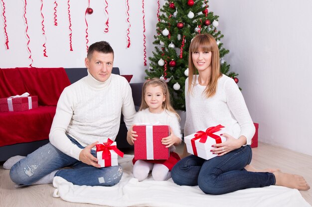 Heureuse jeune famille assise avec des coffrets cadeaux devant l'arbre de Noël