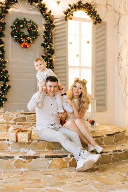 Heureuse jeune famille assise sur le porche de la maison décorée pour Noël