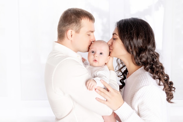 Heureuse jeune famille avec bébé nouveau-né à la maison par la fenêtre, heureux concept de famille aimante