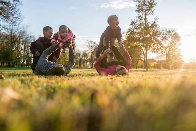 Photo heureuse jeune famille de cinq personnes jouant dans le parc d'automne allongé dans l'herbe profitant de leur temps ensemble