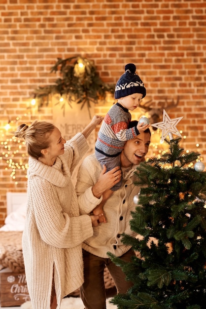 Heureuse jeune famille dans la chambre décore le sapin de Noël