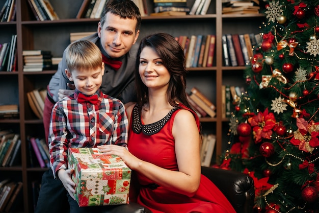 Heureuse jeune famille dans les décorations de Noël, maman, papa et petit garçon près de l'arbre de Noël avec des cadeaux près