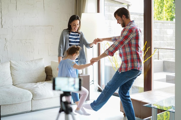 Heureuse Jeune Famille Dansant à La Maison Avec Sa Petite Fille Mignonne, Filmant Une Vidéo.