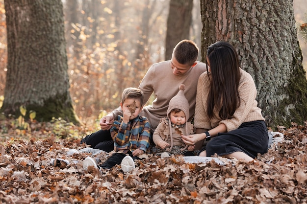 Photo heureuse jeune famille avec deux petits enfants se détendre et s'amuser dans le parc d'automne aux beaux jours