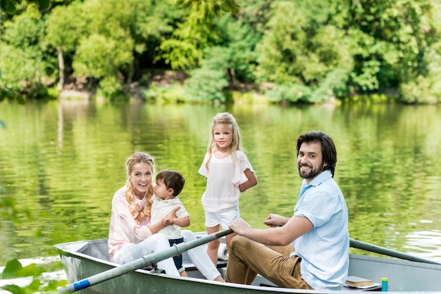 Heureuse jeune famille faisant du bateau sur le lac au parc et regardant la caméra