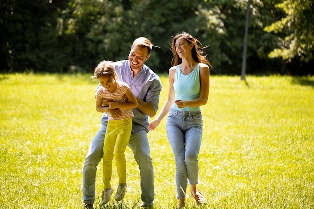 Heureuse jeune famille avec une jolie petite fille qui court dans le parc par une journée ensoleillée