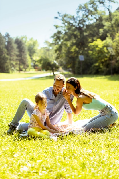 Heureuse jeune famille avec une jolie petite fille s'amusant dans le parc par une journée ensoleillée