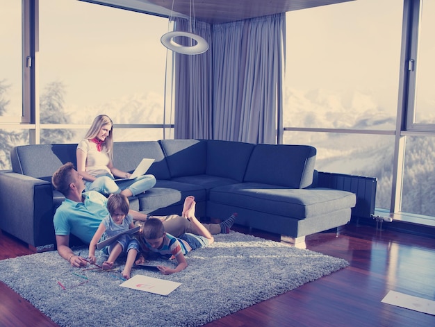 Heureuse jeune famille jouant ensemble à la maison sur le sol à l'aide d'un ordinateur portable et d'un ensemble de dessins pour enfants