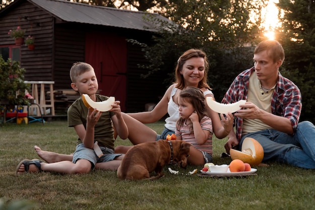 Heureuse jeune famille mangeant du melon dans le jardin ensemble