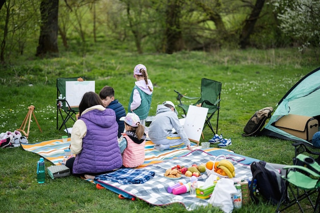 Heureuse jeune famille quatre enfants s'amusant et profitant de la peinture de couverture de pique-nique en plein air au jardin printemps parc détente