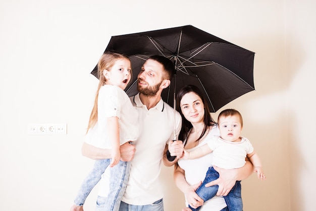 Heureuse jeune famille se sentant en sécurité debout sous un parapluie. Jeune père et mère tenant leurs enfants debout sous un parapluie