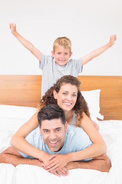 Heureuse jeune famille souriant à la caméra sur le lit posant