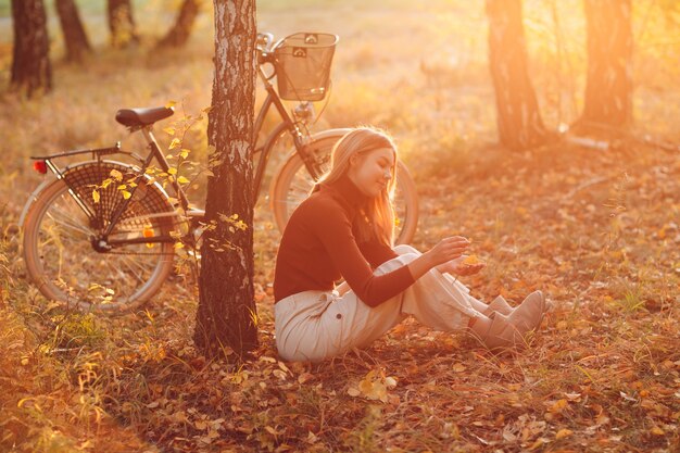 Heureuse jeune femme active assise avec un vélo vintage dans un parc en automne au coucher du soleil