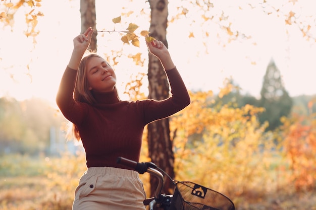 Photo heureuse jeune femme active équitation vélo vintage en automne parc au coucher du soleil