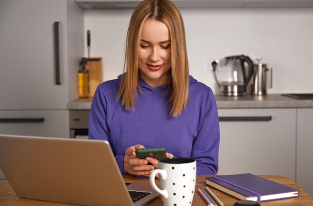 Heureuse jeune femme adulte étude de travail dans la cuisine à l'aide d'un ordinateur portable éducation à distance