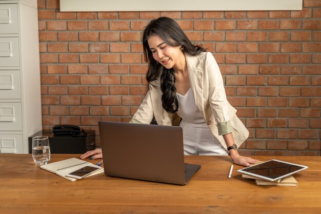 Heureuse jeune femme d'affaires asiatique belle réussie debout et en regardant son ordinateur portable