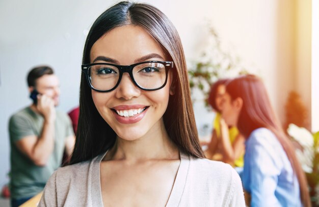 Heureuse jeune femme d'affaires asiatique confiante en vêtements décontractés intelligents pose sur fond d'équipe commerciale moderne. Collègues de travail. Équipe de démarrage. Étudiants ensemble