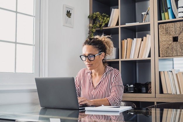 Heureuse jeune femme d'affaires caucasienne souriante travaillant en ligne en regardant un podcast de webinaire sur un ordinateur portable et en apprenant la conférence de cours d'éducation prendre des notes s'asseoir au bureau, concept d'apprentissage en ligne