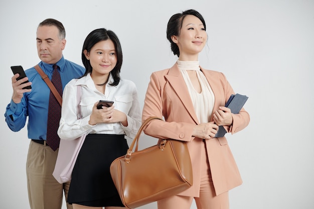 Heureuse jeune femme d'affaires fière debout avec une tablette, ses collègues avec des smartphones debout derrière