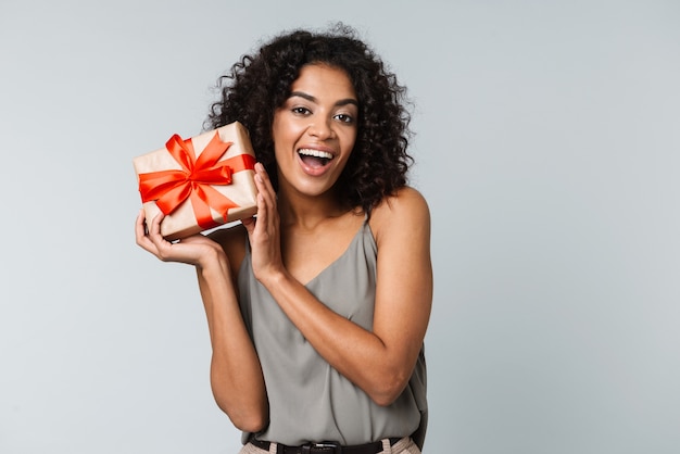 Heureuse jeune femme africaine habillée avec désinvolture debout isolé, tenant une boîte-cadeau