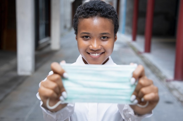 Heureuse jeune femme africaine souriante portant un masque facial en public extérieur