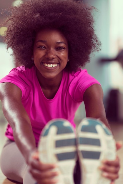 heureuse jeune femme afro-américaine dans une salle de sport qui s'étire et s'échauffe avant l'entraînement