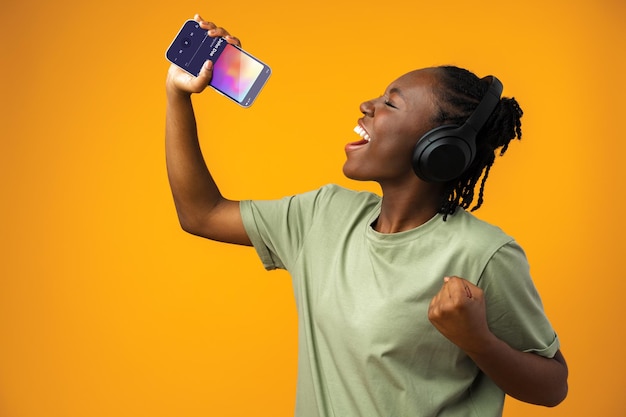 Heureuse jeune femme afro-américaine écoutant de la musique dans des écouteurs sur fond jaune