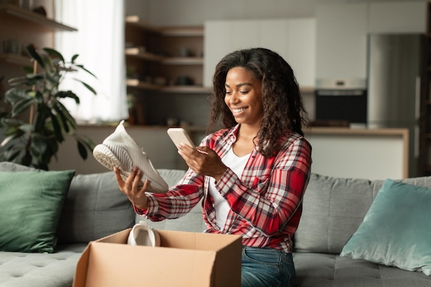 Heureuse jeune femme afro-américaine ouvre la boîte prend des photos de chaussures sur smartphone aime faire des achats en ligne