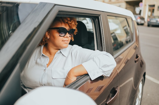 Heureuse jeune femme afro-américaine souriante conducteur aux cheveux afro rouge dans des lunettes de soleil assis dans le nouveau