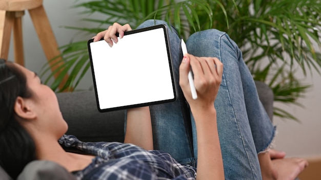 Heureuse jeune femme allongée sur le canapé et utilisant une tablette numérique.