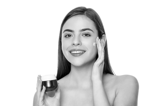 Heureuse jeune femme appliquant de la crème pour la peau du visage isolée sur fond blanc soins personnels