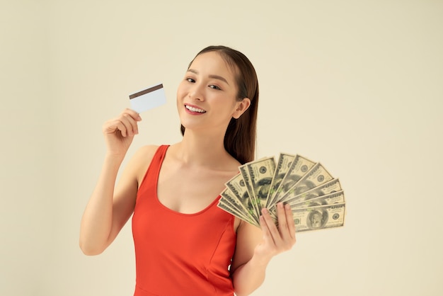 Heureuse jeune femme avec de l'argent liquide et une carte de crédit sur fond gris