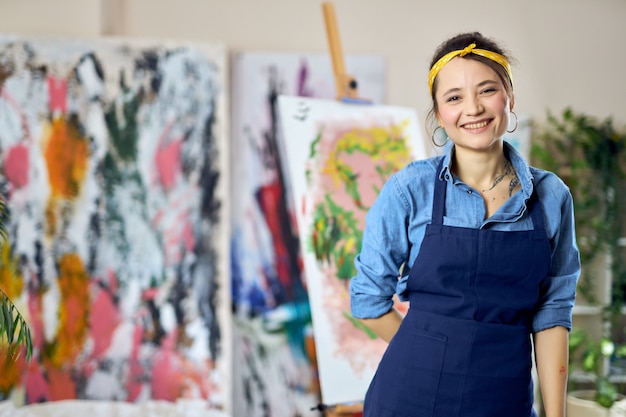 Heureuse jeune femme artiste féminine en tablier souriant à la caméra posant à l'atelier home studio