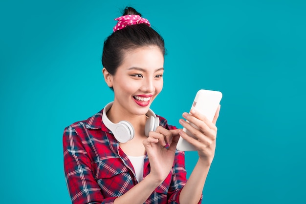 Heureuse jeune femme asiatique à l'aide de smartphone debout sur bleu.