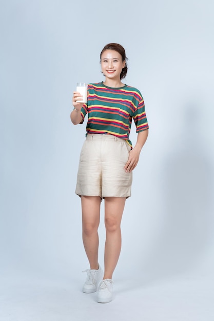 Heureuse jeune femme asiatique, boire du lait du verre sur fond blanc secouer en regardant la caméra