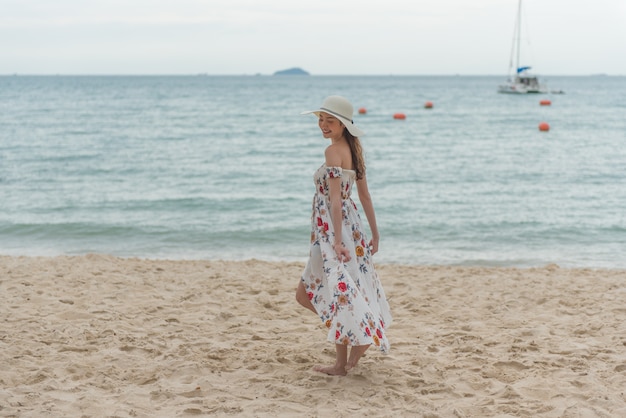 Heureuse jeune femme asiatique avec un chapeau à pied et se détendre sur la plage de sable avec bonheur.